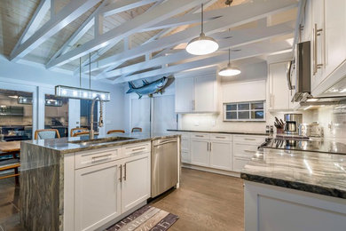 Inspiration for a mid-sized coastal l-shaped medium tone wood floor and gray floor eat-in kitchen remodel in Miami with a single-bowl sink, shaker cabinets, white cabinets, quartzite countertops, gray backsplash, glass tile backsplash, stainless steel appliances, an island and gray countertops