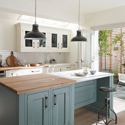 Kitchen - traditional light wood floor kitchen idea in London with recessed-panel cabinets, white cabinets, white backsplash, subway tile backsplash, stainless steel appliances and an island