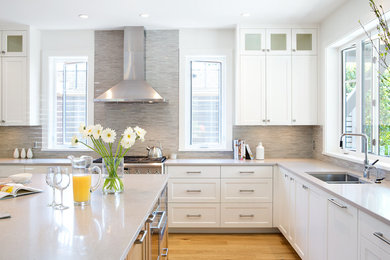 Eat-in kitchen - large transitional l-shaped medium tone wood floor and brown floor eat-in kitchen idea in Vancouver with an undermount sink, shaker cabinets, white cabinets, quartz countertops, gray backsplash, matchstick tile backsplash, stainless steel appliances, an island and gray countertops