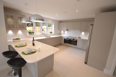 This is an example of a large contemporary u-shaped open plan kitchen in Surrey with a double-bowl sink, shaker cabinets, grey cabinets, quartz worktops, grey splashback, stone slab splashback, stainless steel appliances, ceramic flooring and a breakfast bar.