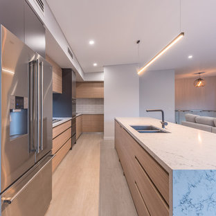 Inspiration for a contemporary galley open plan kitchen in Perth with an undermount sink, flat-panel cabinets, medium wood cabinets, quartz benchtops, white splashback, subway tile splashback, stainless steel appliances, light hardwood floors, with island and beige floor.