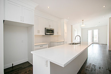 Kitchen - mid-sized transitional galley dark wood floor and gray floor kitchen idea in Toronto with shaker cabinets, white cabinets, quartzite countertops, an island and a double-bowl sink