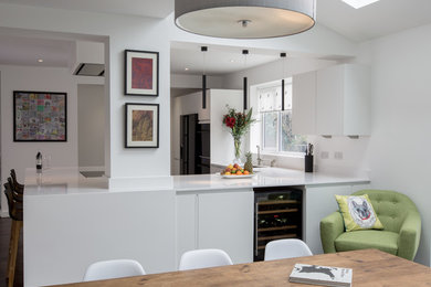 Inspiration for a medium sized contemporary u-shaped open plan kitchen in London with a submerged sink, flat-panel cabinets, white cabinets, composite countertops, black appliances, dark hardwood flooring and a breakfast bar.