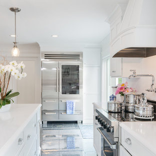 Photo of a beach style kitchen in Manchester with a farmhouse sink, flat-panel cabinets, white cabinets, quartz benchtops, white splashback, stainless steel appliances, ceramic floors, with island, grey floor and white benchtop.