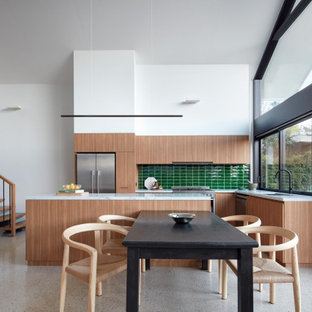 Mid-sized contemporary l-shaped open plan kitchen in Melbourne with a double-bowl sink, flat-panel cabinets, medium wood cabinets, green splashback, glass tile splashback, stainless steel appliances, with island, grey floor and white benchtop.