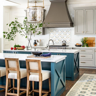 Modelo de cocina comedor de galera, de estilo de casa de campo, con fregadero bajoencimera, armarios con paneles empotrados, puertas de armario turquesas, salpicadero blanco, salpicadero de azulejos tipo metro, electrodomésticos de acero inoxidable, suelo de madera en tonos medios, dos o más islas, suelo marrón y encimeras blancas