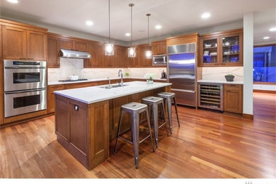 Large l-shaped light wood floor eat-in kitchen photo in Seattle with an undermount sink, brown cabinets, quartz countertops, white backsplash, stone slab backsplash, stainless steel appliances and an island