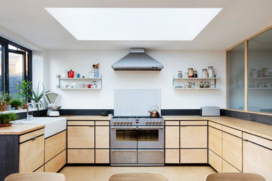 Scandi l-shaped kitchen/diner in London with a belfast sink, flat-panel cabinets, light wood cabinets, wood worktops, stainless steel appliances, cork flooring, beige floors and no island.