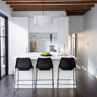Photo of a mid-sized transitional open plan kitchen in Sydney with a drop-in sink, shaker cabinets, white cabinets, white splashback, dark hardwood floors, with island, brown floor, white benchtop and exposed beam.