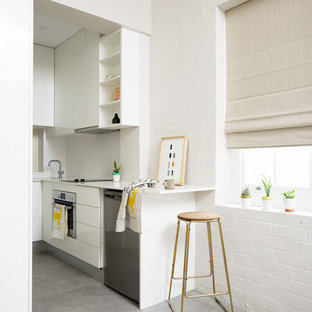 Photo of a small contemporary kitchen in Brisbane with white cabinets, stainless steel appliances, flat-panel cabinets, white splashback, glass sheet splashback and concrete floors.