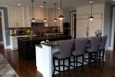 Inspiration for a large transitional l-shaped dark wood floor open concept kitchen remodel in Cleveland with an undermount sink, raised-panel cabinets, white cabinets, granite countertops, gray backsplash, glass tile backsplash, stainless steel appliances and two islands