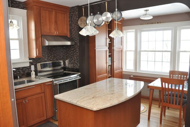This is an example of a small traditional l-shaped kitchen/diner in Providence with raised-panel cabinets, medium wood cabinets, black appliances, an island, a submerged sink, light hardwood flooring and beige floors.