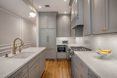 Kitchen - small transitional l-shaped medium tone wood floor and beige floor kitchen idea in New York with recessed-panel cabinets, gray cabinets, white backsplash, stainless steel appliances, an island, an undermount sink, quartzite countertops, stone slab backsplash and white countertops