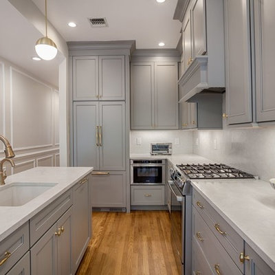 Kitchen - small transitional l-shaped medium tone wood floor and beige floor kitchen idea in New York with recessed-panel cabinets, gray cabinets, white backsplash, stainless steel appliances, an island, an undermount sink, quartzite countertops, stone slab backsplash and white countertops