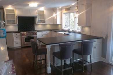 Transitional u-shaped kitchen photo in New York with a farmhouse sink, recessed-panel cabinets, white cabinets, white backsplash and a peninsula