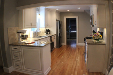 Example of a mid-sized classic l-shaped light wood floor eat-in kitchen design in Boston with an undermount sink, raised-panel cabinets, white cabinets, granite countertops, beige backsplash, marble backsplash and stainless steel appliances