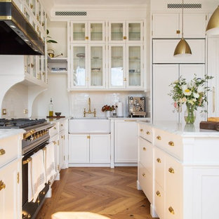 Idee per una cucina a L minimalista con lavello stile country, ante in stile shaker, ante bianche, paraspruzzi bianco, elettrodomestici da incasso, pavimento in legno massello medio, isola, pavimento marrone e top bianco