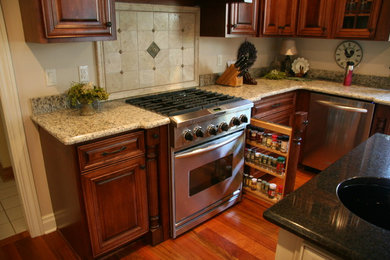 Example of a mid-sized classic l-shaped dark wood floor and brown floor kitchen design in Milwaukee with a single-bowl sink, raised-panel cabinets, dark wood cabinets, granite countertops, beige backsplash, ceramic backsplash, stainless steel appliances and an island