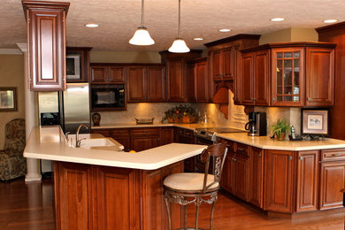Photo of a large traditional kitchen/diner in Nashville with an integrated sink, raised-panel cabinets, medium wood cabinets, composite countertops, beige splashback, porcelain splashback, stainless steel appliances, medium hardwood flooring and an island.