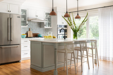 Mid-sized transitional galley light wood floor kitchen photo in Boston with shaker cabinets, white cabinets, blue backsplash, ceramic backsplash, stainless steel appliances, white countertops and an island
