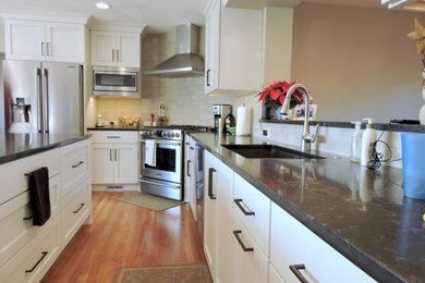 Example of a large classic l-shaped medium tone wood floor and brown floor eat-in kitchen design in Other with an undermount sink, recessed-panel cabinets, white cabinets, quartzite countertops, beige backsplash, ceramic backsplash, stainless steel appliances, an island and brown countertops