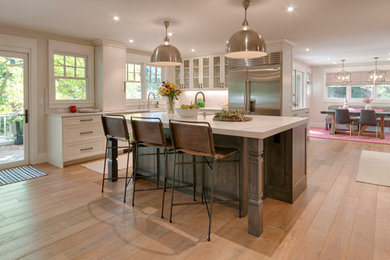 Example of a country l-shaped medium tone wood floor and brown floor kitchen design in Denver with a farmhouse sink, shaker cabinets, white cabinets, stainless steel appliances, an island and white countertops