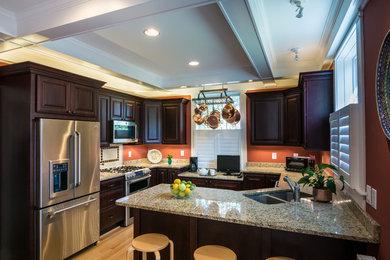 Mid-sized elegant u-shaped light wood floor enclosed kitchen photo in Baltimore with an undermount sink, raised-panel cabinets, dark wood cabinets, marble countertops, stainless steel appliances and a peninsula