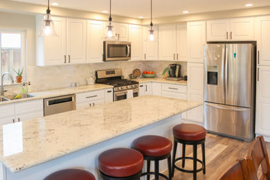 Mid-sized beach style l-shaped vinyl floor and beige floor kitchen photo in Orange County with an undermount sink, raised-panel cabinets, white cabinets, granite countertops, beige backsplash, travertine backsplash, stainless steel appliances, an island and white countertops