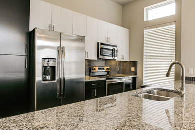 Example of a mid-sized transitional single-wall eat-in kitchen design in Houston with a double-bowl sink, flat-panel cabinets, black cabinets, granite countertops, black backsplash, glass tile backsplash, stainless steel appliances and an island