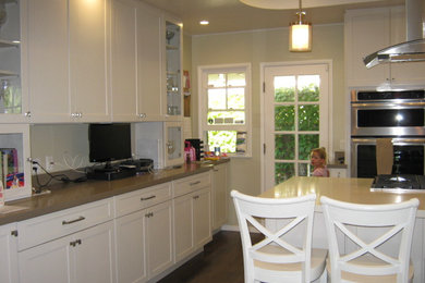 Kitchen - mid-sized transitional u-shaped medium tone wood floor kitchen idea in Los Angeles with a farmhouse sink, shaker cabinets, white cabinets, quartz countertops, white backsplash, ceramic backsplash, stainless steel appliances and an island