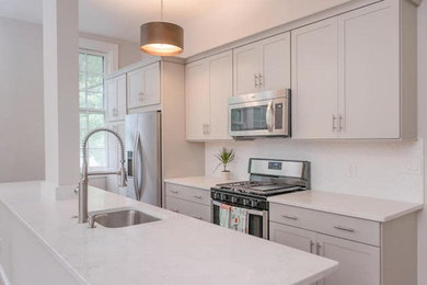 Example of a trendy galley medium tone wood floor and brown floor open concept kitchen design in DC Metro with an undermount sink, recessed-panel cabinets, white cabinets, solid surface countertops, white backsplash, stainless steel appliances and an island