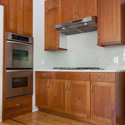 Large cottage u-shaped light wood floor eat-in kitchen photo in DC Metro with a farmhouse sink, shaker cabinets, medium tone wood cabinets, quartzite countertops, gray backsplash, ceramic backsplash, stainless steel appliances and a peninsula