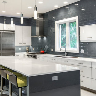 Contemporary eat-in kitchen ideas - Inspiration for a contemporary l-shaped porcelain tile eat-in kitchen remodel in Miami with gray backsplash, glass tile backsplash, stainless steel appliances, flat-panel cabinets, white cabinets, an undermount sink, an island and solid surface countertops