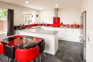 Diseño de cocina actual de tamaño medio con salpicadero rojo, electrodomésticos de acero inoxidable, suelo de baldosas de cerámica y una isla