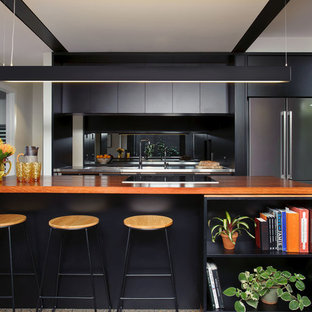 This is an example of a mid-sized contemporary galley open plan kitchen in Brisbane with an integrated sink, flat-panel cabinets, black cabinets, wood benchtops, stainless steel appliances, concrete floors, multiple islands, mirror splashback and grey floor.