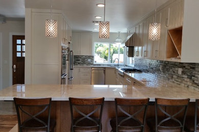 Example of a mid-sized transitional u-shaped medium tone wood floor and brown floor eat-in kitchen design in Los Angeles with an undermount sink, shaker cabinets, white cabinets, multicolored backsplash, glass tile backsplash, stainless steel appliances, marble countertops and a peninsula