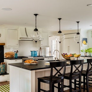 Large transitional eat-in kitchen ideas - Large transitional l-shaped medium tone wood floor and brown floor eat-in kitchen photo in Boston with a farmhouse sink, flat-panel cabinets, white cabinets, soapstone countertops, white backsplash, subway tile backsplash, paneled appliances and an island