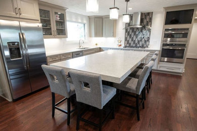 Mid-sized transitional l-shaped medium tone wood floor and red floor eat-in kitchen photo in Cleveland with an undermount sink, recessed-panel cabinets, gray cabinets, quartz countertops, white backsplash, porcelain backsplash, stainless steel appliances, an island and white countertops
