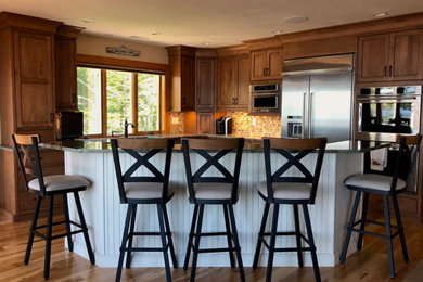 Inspiration for a large transitional l-shaped medium tone wood floor and brown floor kitchen remodel in Boston with medium tone wood cabinets, an island, a farmhouse sink, shaker cabinets, granite countertops, multicolored backsplash, glass tile backsplash and stainless steel appliances