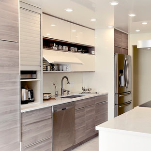 Immagine di una cucina minimalista di medie dimensioni con lavello sottopiano, ante lisce, ante in legno chiaro, top in quarzo composito, elettrodomestici in acciaio inossidabile e isola