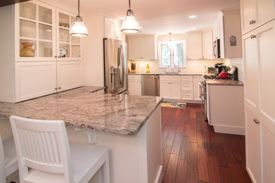 Photo of a kitchen in Boston with a single-bowl sink, white cabinets, granite worktops, white splashback, stainless steel appliances, medium hardwood flooring and a breakfast bar.