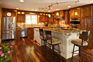 This is an example of a large traditional l-shaped kitchen/diner in Minneapolis with a submerged sink, raised-panel cabinets, dark wood cabinets, granite worktops, beige splashback, ceramic splashback, stainless steel appliances, dark hardwood flooring, an island and brown floors.
