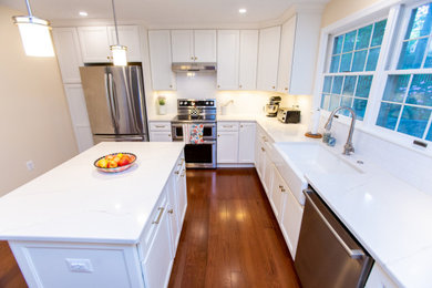 Example of a mid-sized transitional u-shaped dark wood floor and red floor eat-in kitchen design in DC Metro with a farmhouse sink, recessed-panel cabinets, white cabinets, solid surface countertops, white backsplash, porcelain backsplash, stainless steel appliances, an island and white countertops
