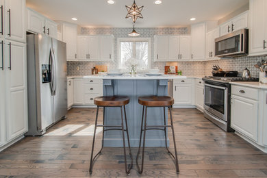 Inspiration for a classic u-shaped kitchen in Grand Rapids with raised-panel cabinets, white cabinets, stainless steel appliances, dark hardwood flooring, an island, brown floors and white worktops.