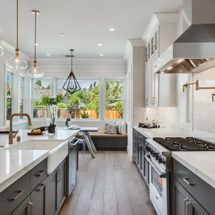 Aménagement d'une grand cuisine ouverte campagne avec un évier de ferme, un placard à porte shaker, des portes de placard grises, un plan de travail en quartz modifié, une crédence blanche, une crédence en quartz modifié, un électroménager en acier inoxydable, un sol en bois clair, un îlot central, un sol gris et un plan de travail blanc.