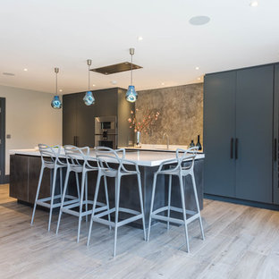 Inspiration for a medium sized contemporary single-wall kitchen in Kent with a submerged sink, flat-panel cabinets, grey splashback, integrated appliances, an island, beige floors, white worktops and blue cabinets.