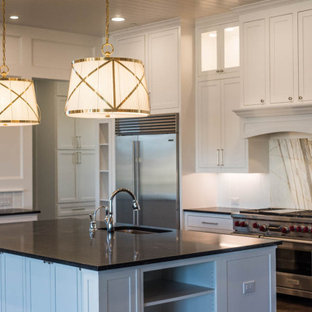 This is an example of an expansive transitional eat-in kitchen in Dallas with a drop-in sink, recessed-panel cabinets, white cabinets, granite benchtops, white splashback, stainless steel appliances, medium hardwood floors, with island, brown floor and black benchtop.