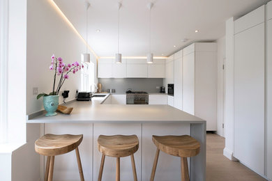 This is an example of a medium sized contemporary u-shaped kitchen with quartz worktops, grey splashback, stainless steel appliances, a breakfast bar, a submerged sink, flat-panel cabinets and white cabinets.