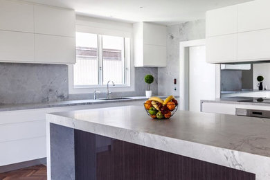 Inredning av ett modernt stort kök, med vita skåp, marmorbänkskiva, stänkskydd i marmor, rostfria vitvaror, en köksö och grått stänkskydd