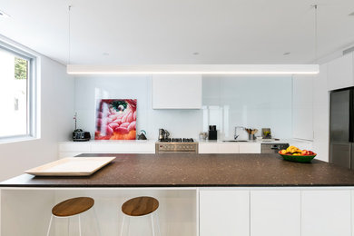 Exempel på ett stort modernt brun brunt kök, med en undermonterad diskho, vita skåp, bänkskiva i kvarts, vitt stänkskydd, glaspanel som stänkskydd, rostfria vitvaror, betonggolv, en köksö och grått golv
